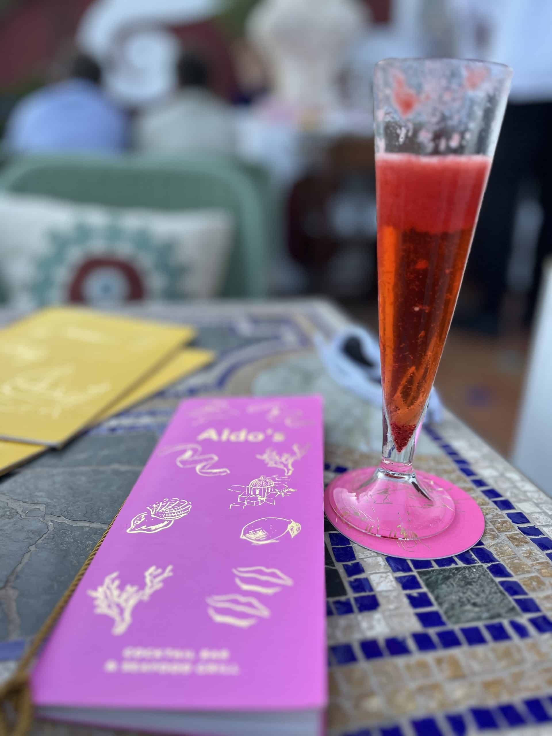 A menu next to a glass of raspberry prosecco