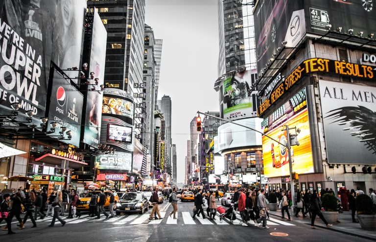 A crowd of people crossing the street in New York near Times Square with large digital billboards and buildings in the background