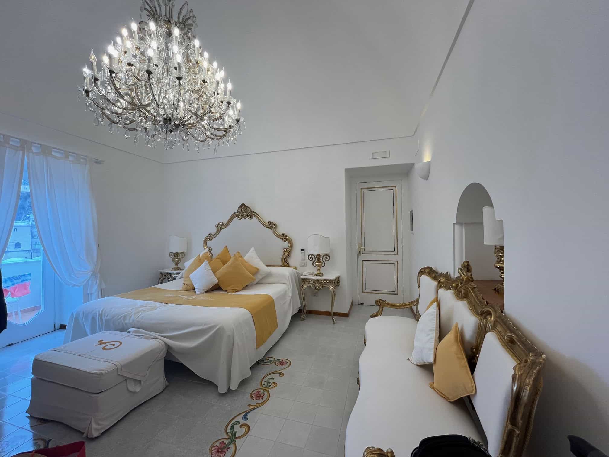 A spacious hotel room with a king size bed, couch and chandelier at Villia Yiara in Positano
