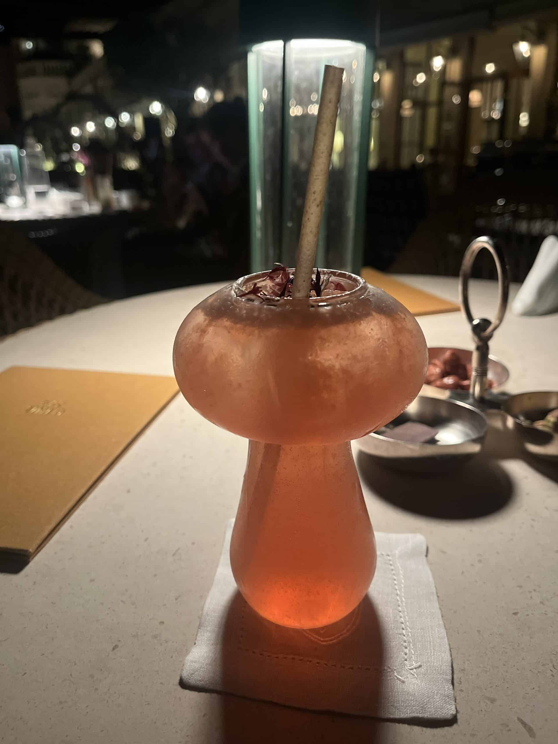 Cocktail drink in an oddly shaped glass with a straw, sitting on a table