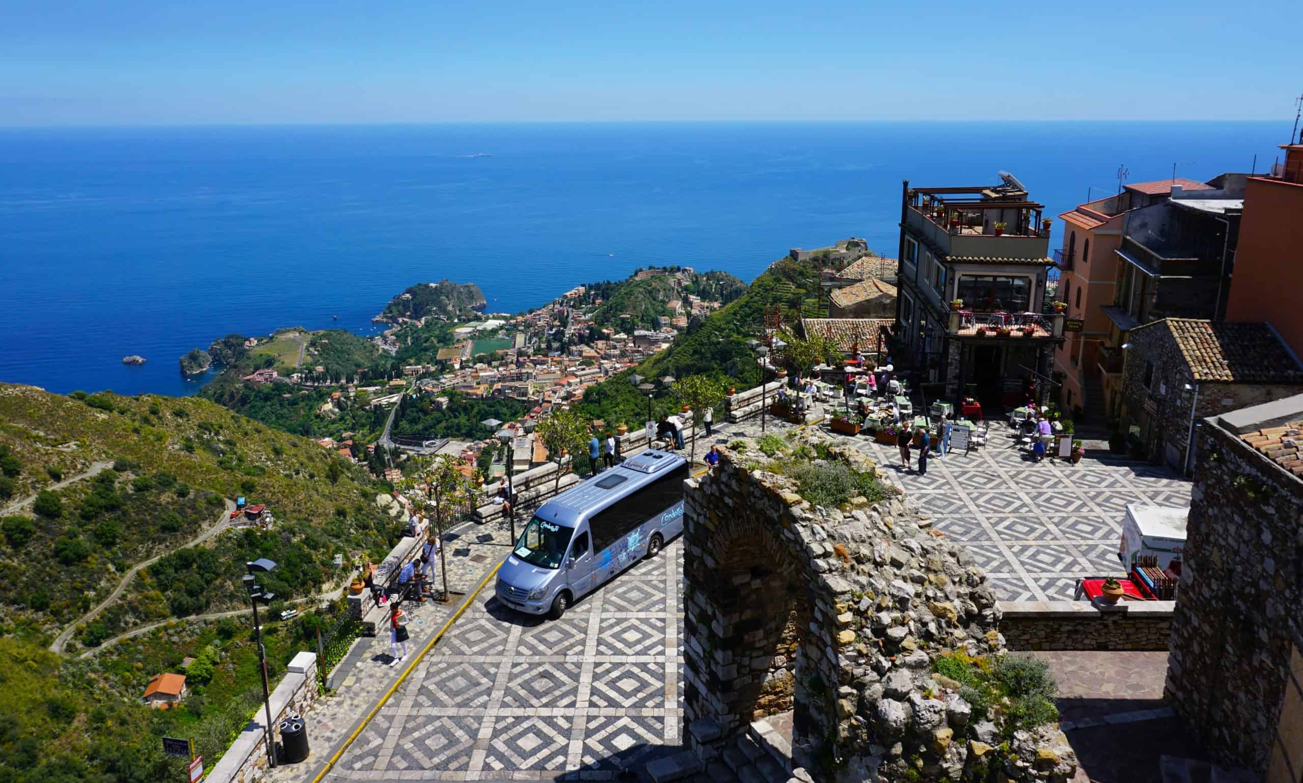 A bus in a piazza overlooking a town on the coastal water
