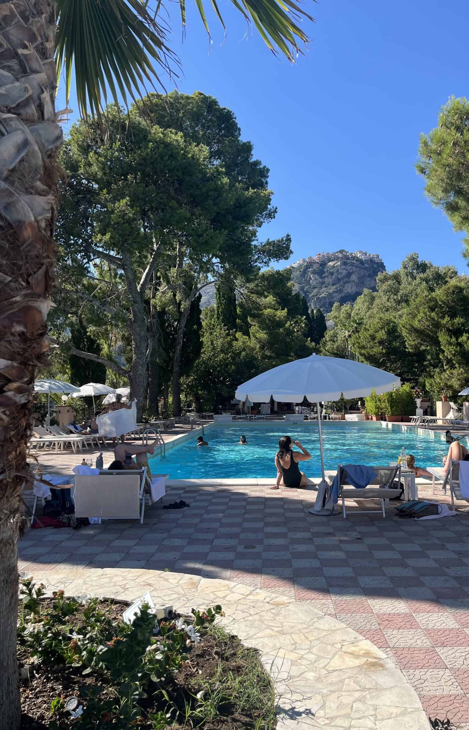 People sitting in front of a pool surrounded by trees and a mountain in the background