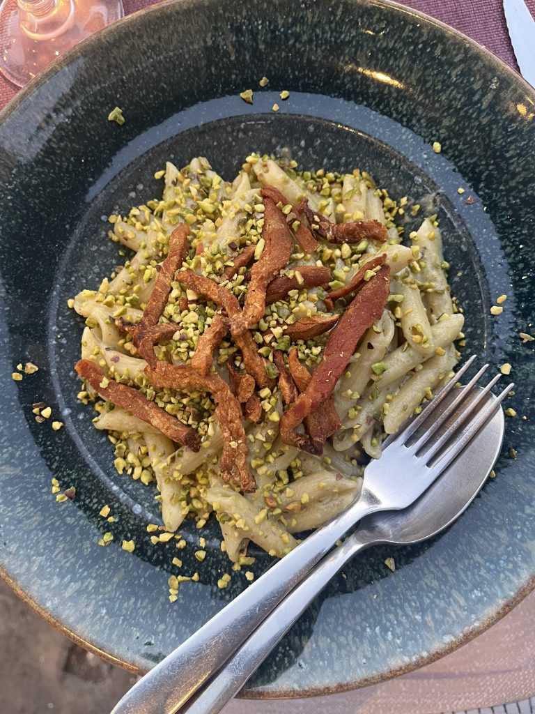 Plate of pasta with pistachios and and meat fork and spoon