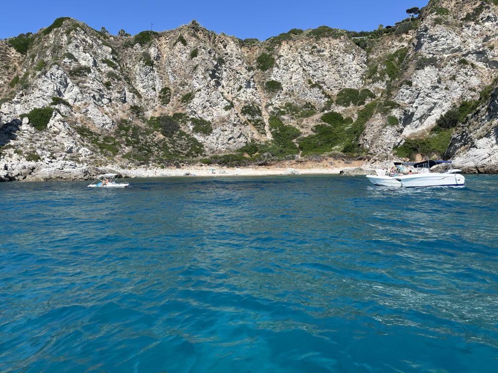 boats in crystal cleaer water in front of a small beach and cliff