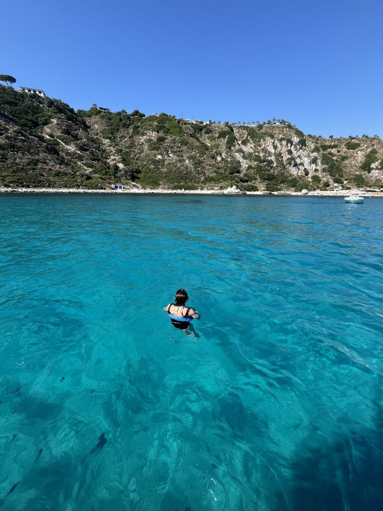 A woman swimming in crystal clear water with cliffs behind
