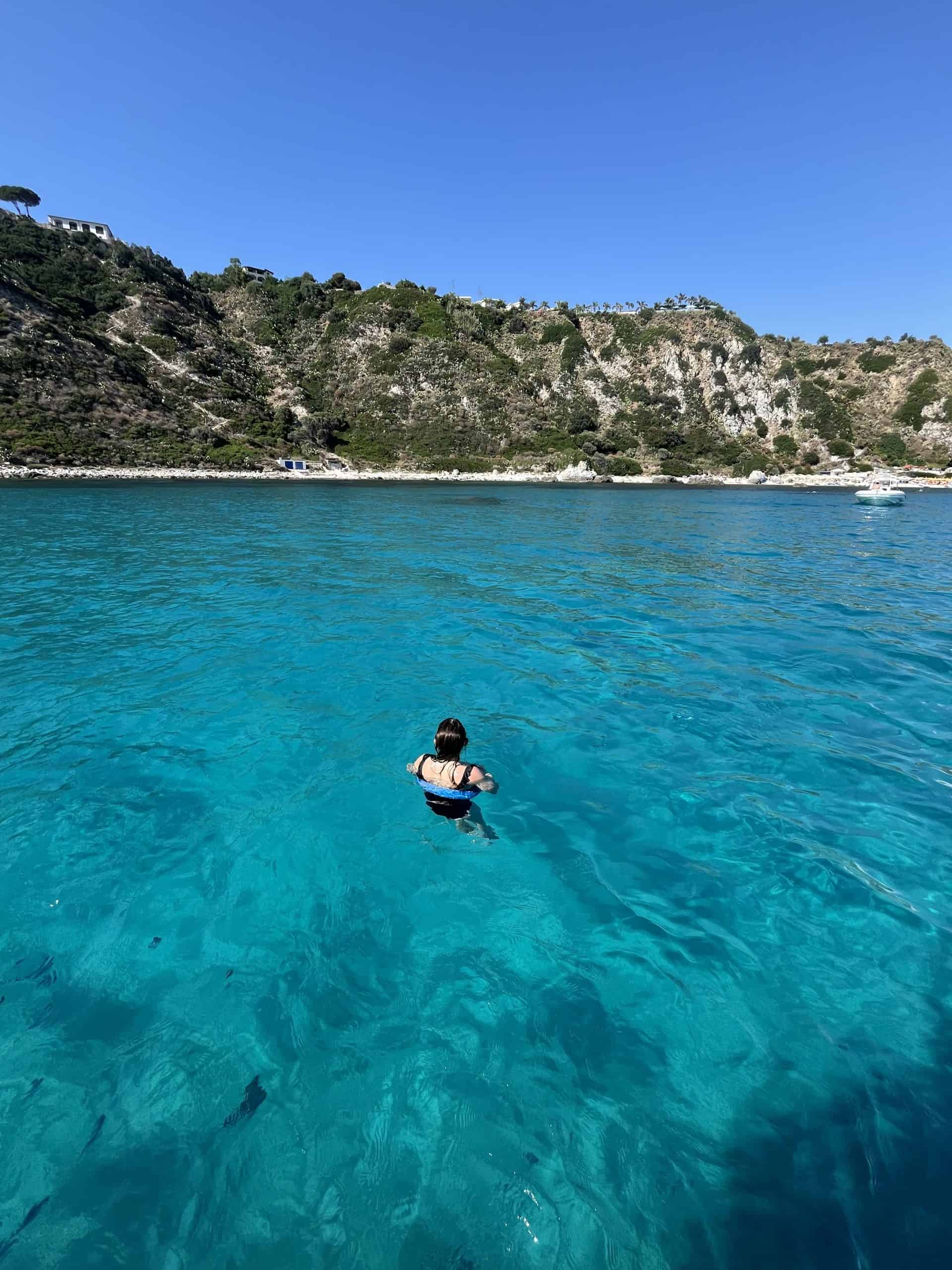 A woman swimming in crystal clear water with cliffs behind