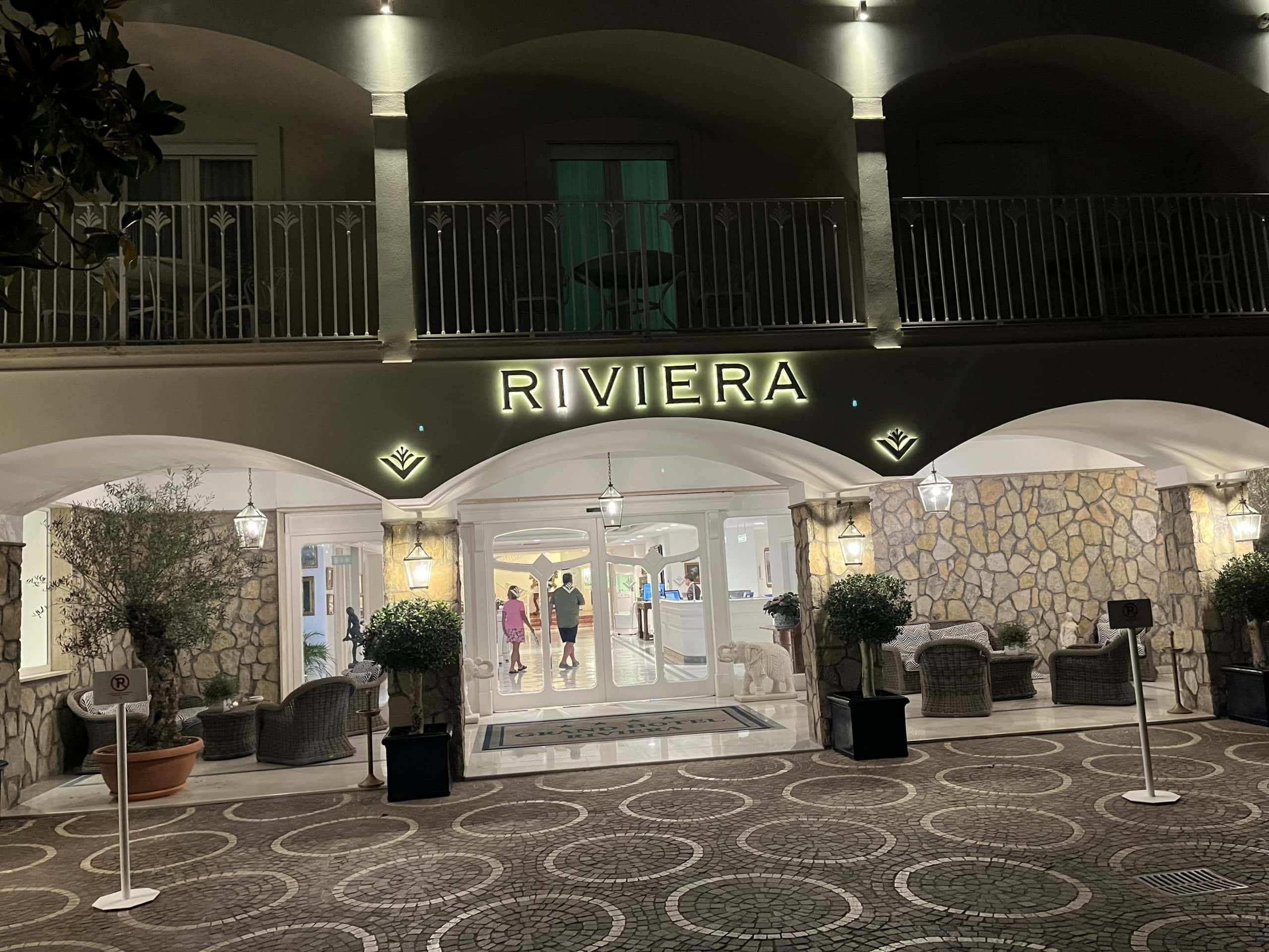 hotel entrance from driveway with small trees on either side and the word Riviera in lights