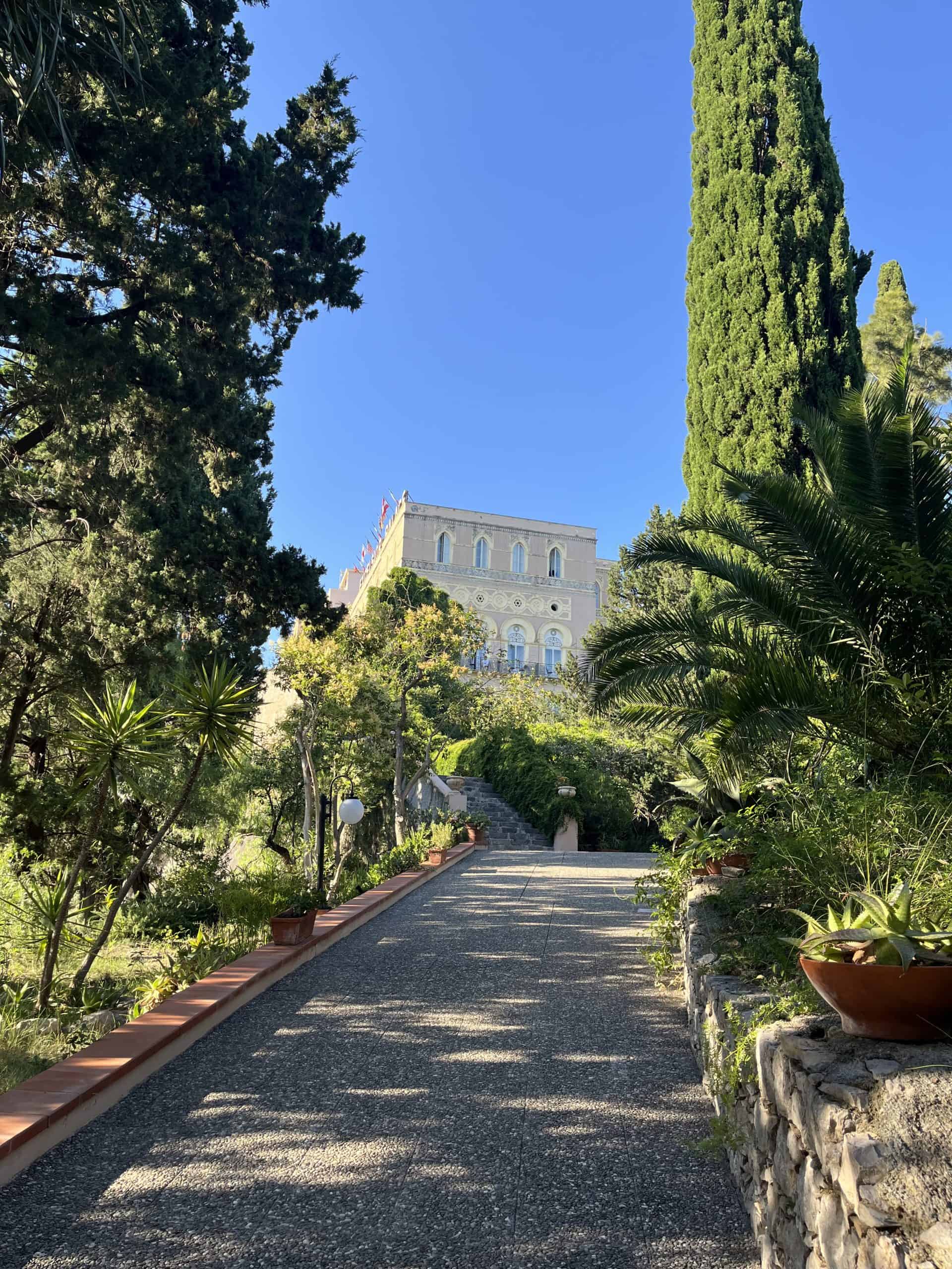 An uphill pathway with trees on either side and a hotel building at the top