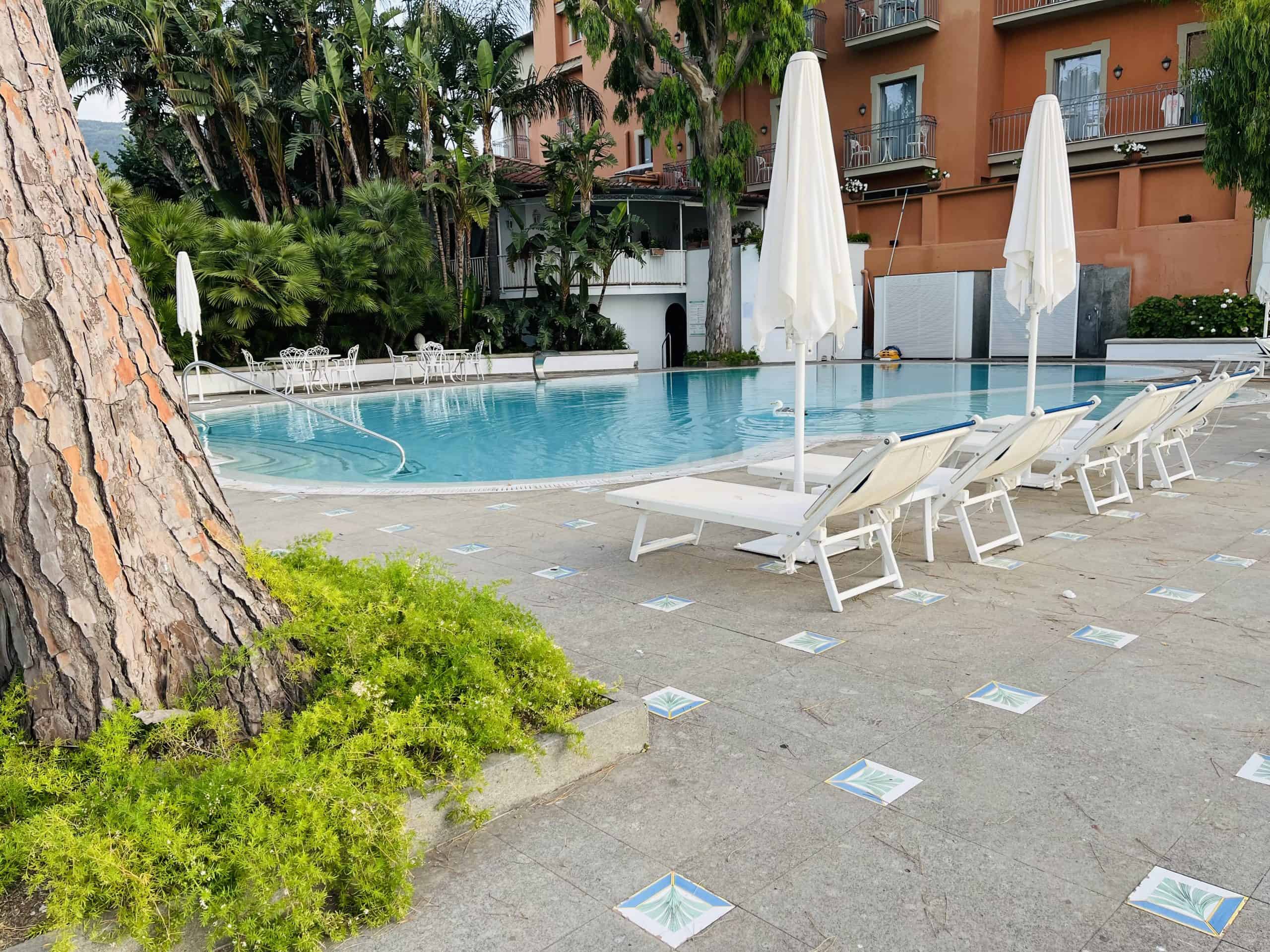 swimming pool with white chairs umbrellas and trees surrounding it
