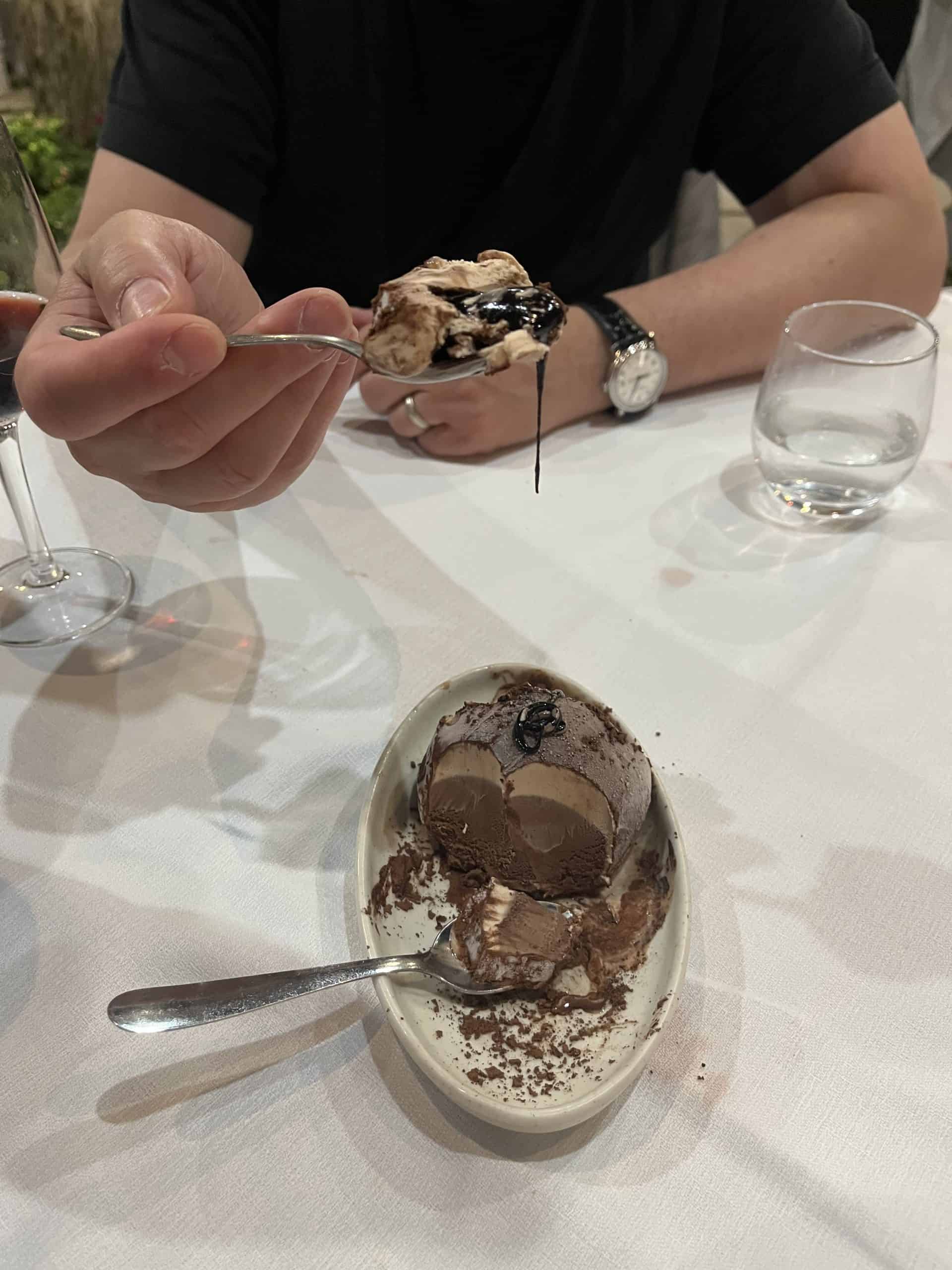 A bowl with chocolate tartufo and a portion of it on a spoon with chocolate syrup
