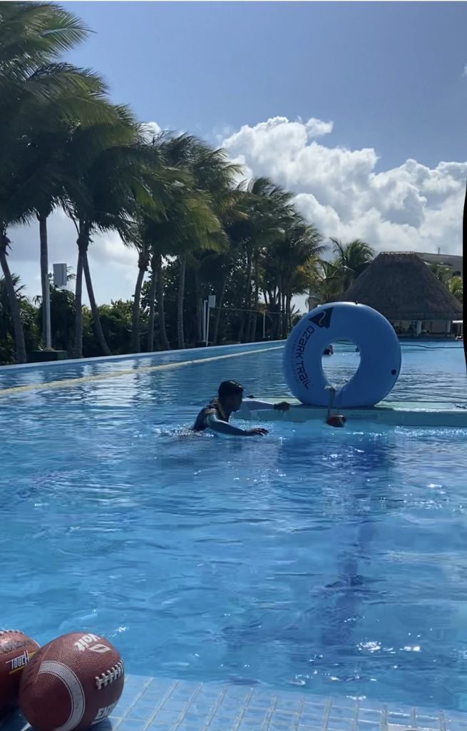 a rectangular pool with a blue inflatable ring floating on water and footballs in the forefront