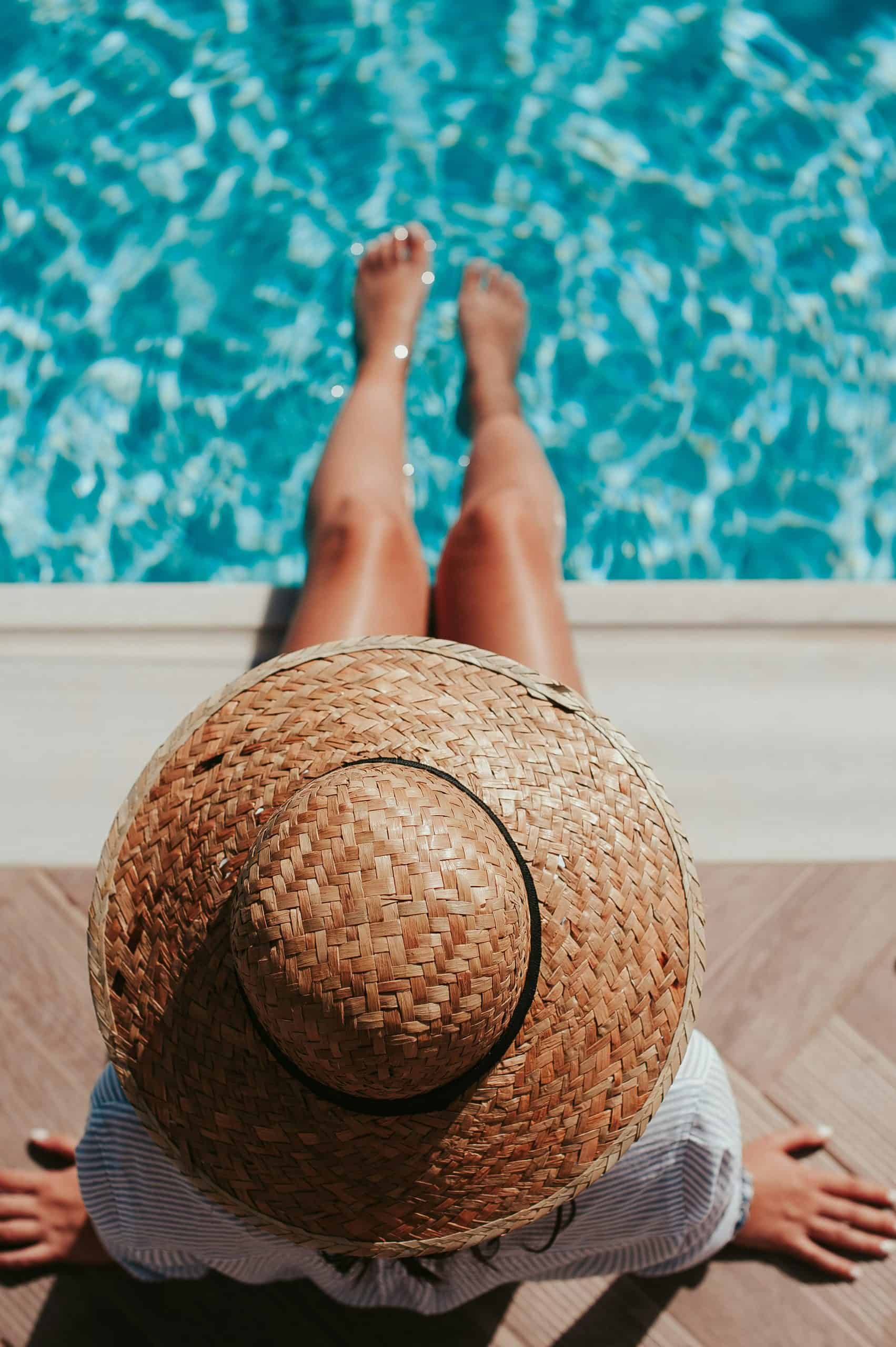 Woman wearing a hat stretching her legs over the pool water