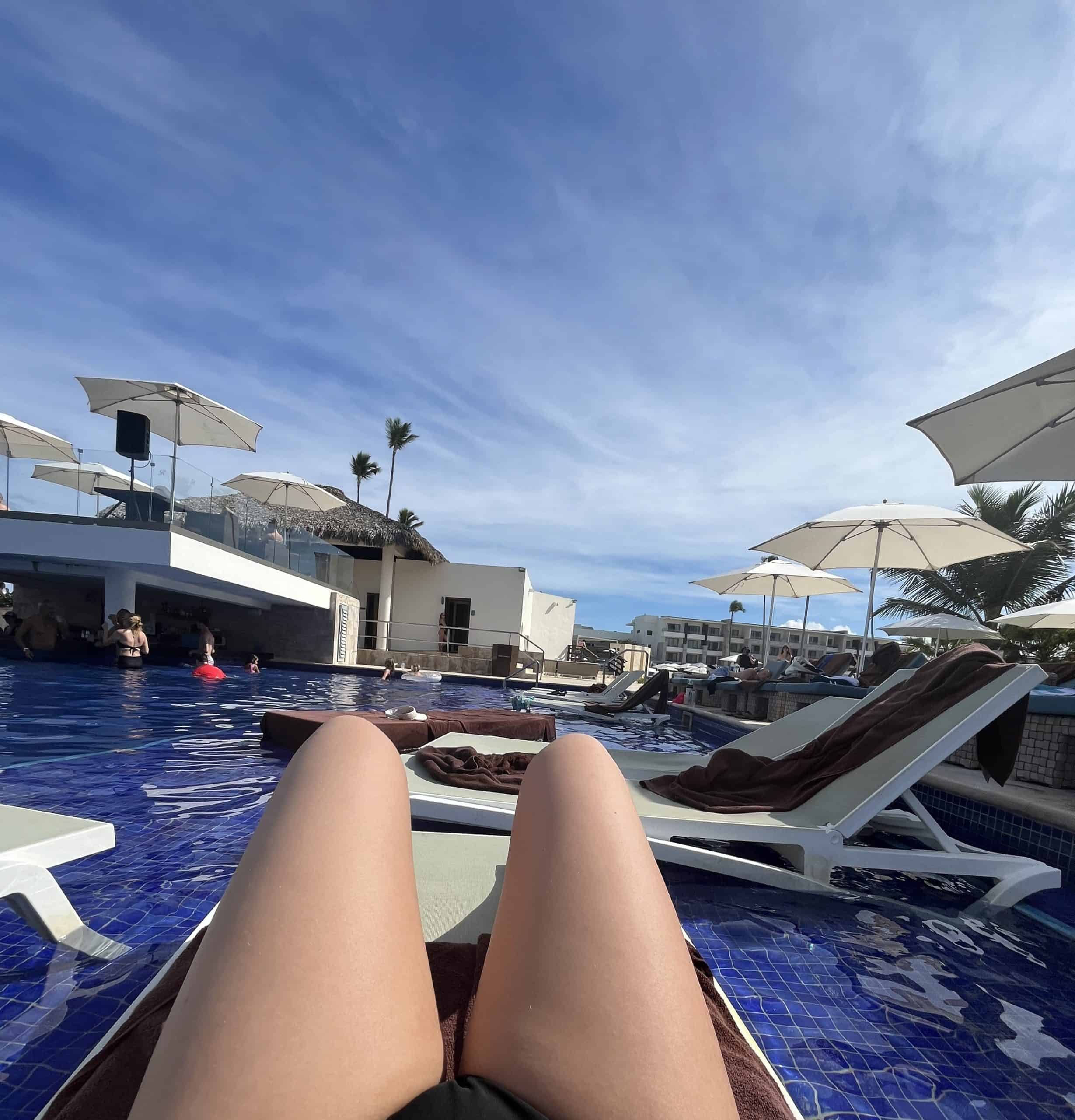 pool chairs on pool deck bent legs in front and blue sky and umbrellas behind
