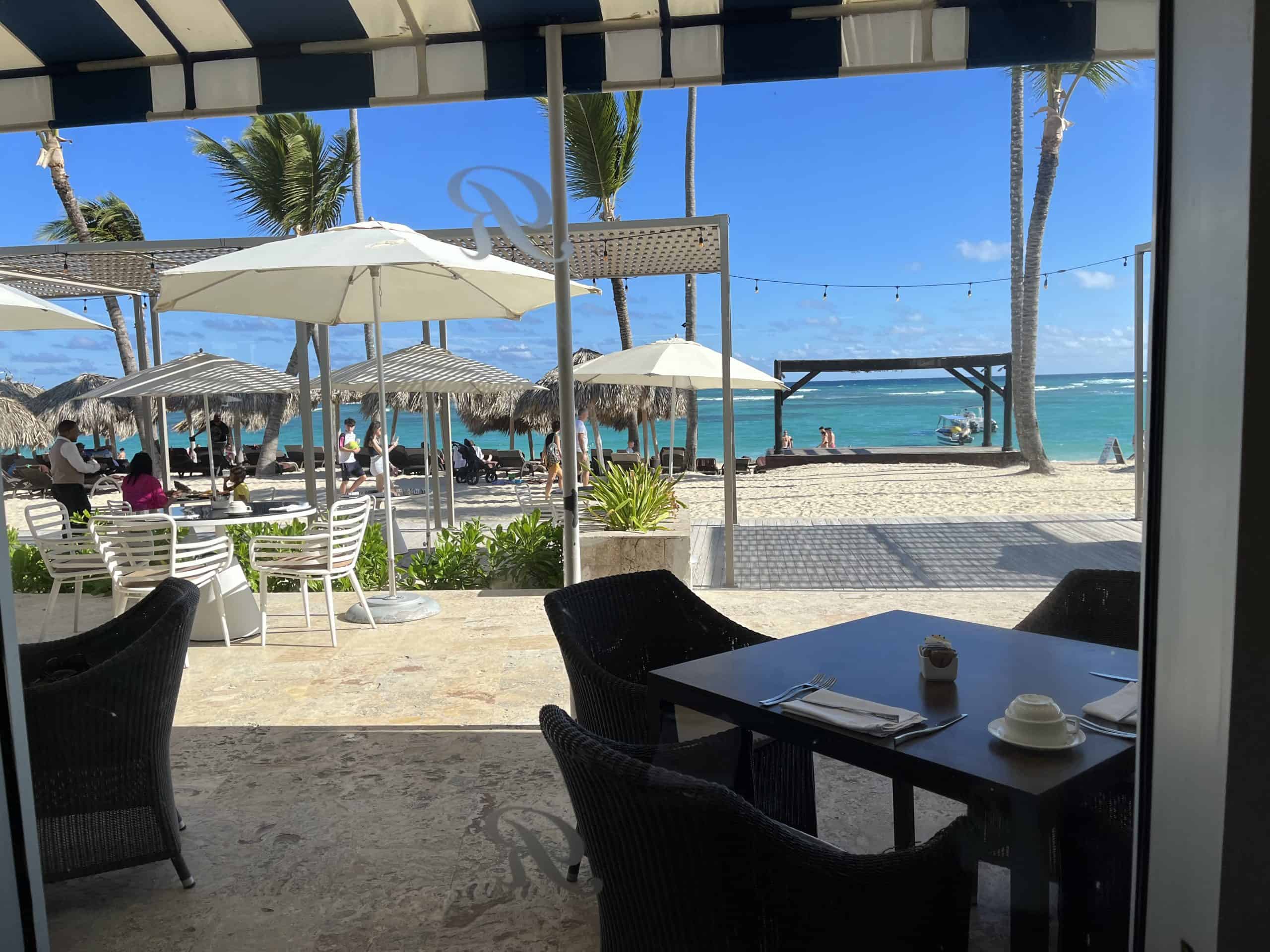 Beach huts, white beach umbrellas and blue sky in background and table with 2 chairs