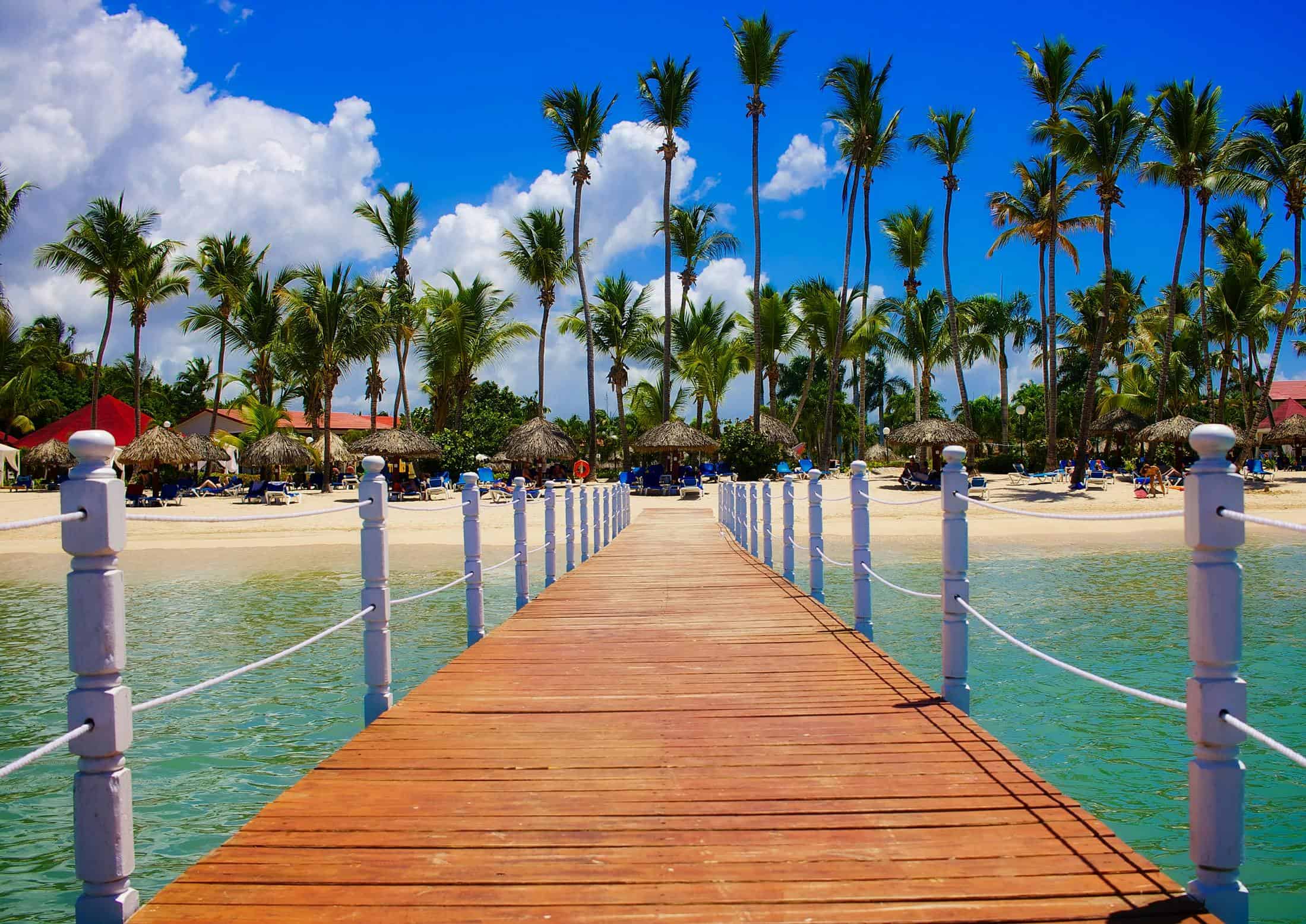 walkway over water to beach with palm trees