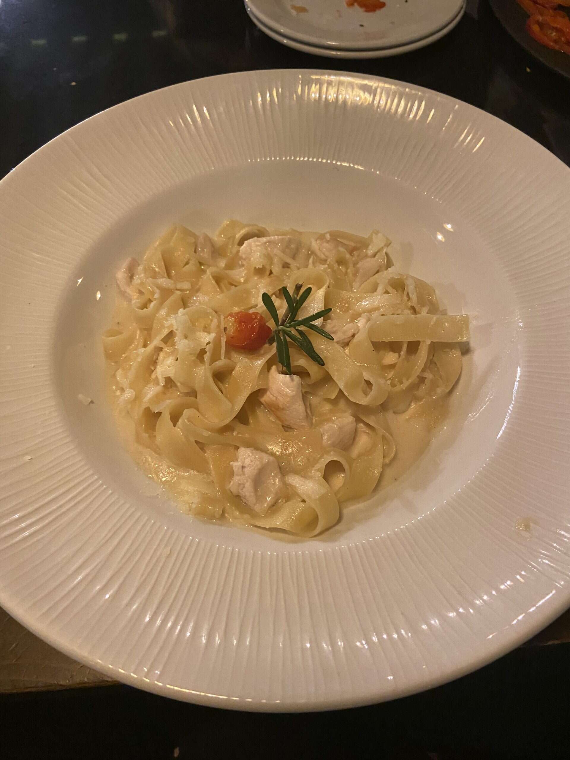 white dish with yellow noodles and green rosemary pieces in a circle