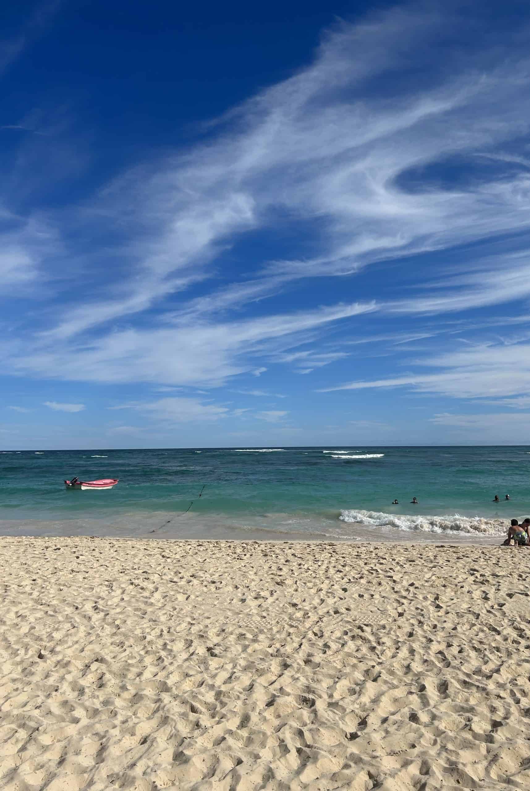 White and blue sky with turquoise water and people in it and on the golden sandy beach