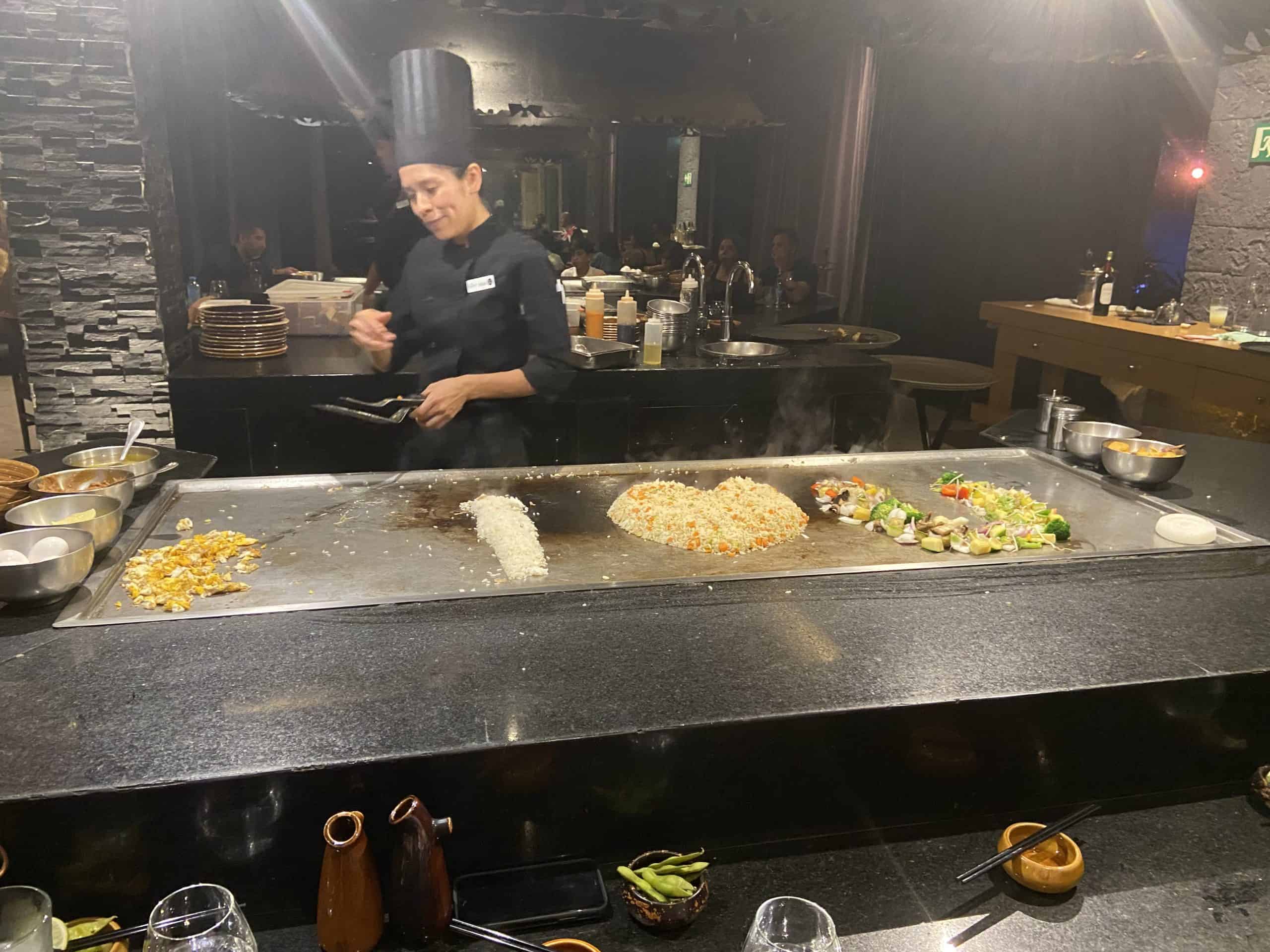 A woman in a chef's uniform grilling food in the shapes of I heart you