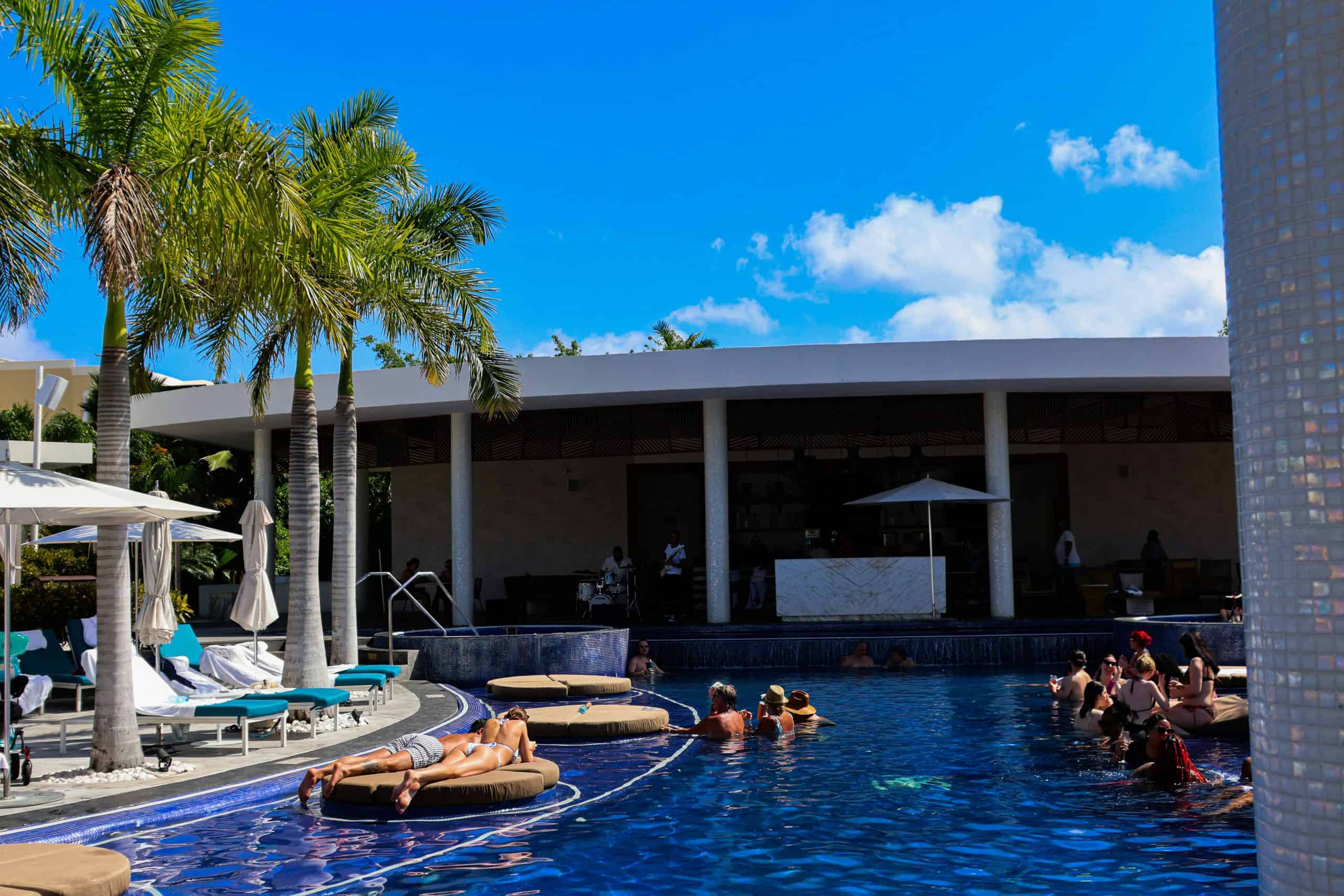 people standing in crowds on either side of the pool and laying down in the pool on pillow platforms