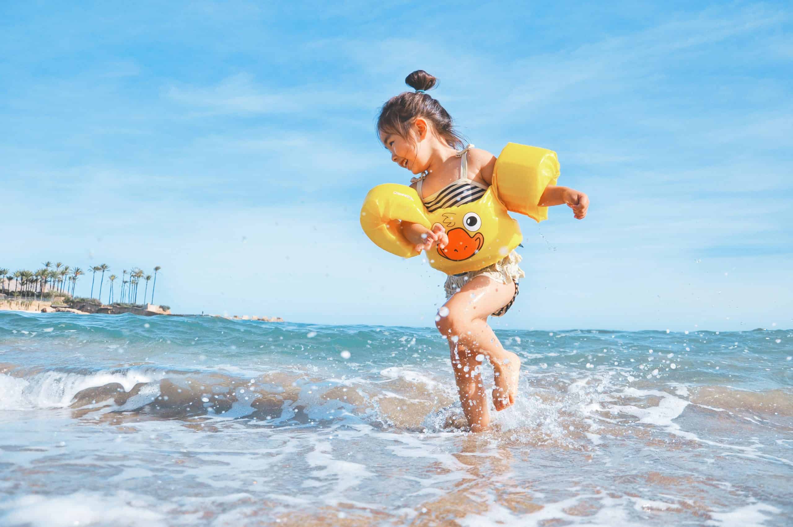 A girl with yellow water wings running in beach water