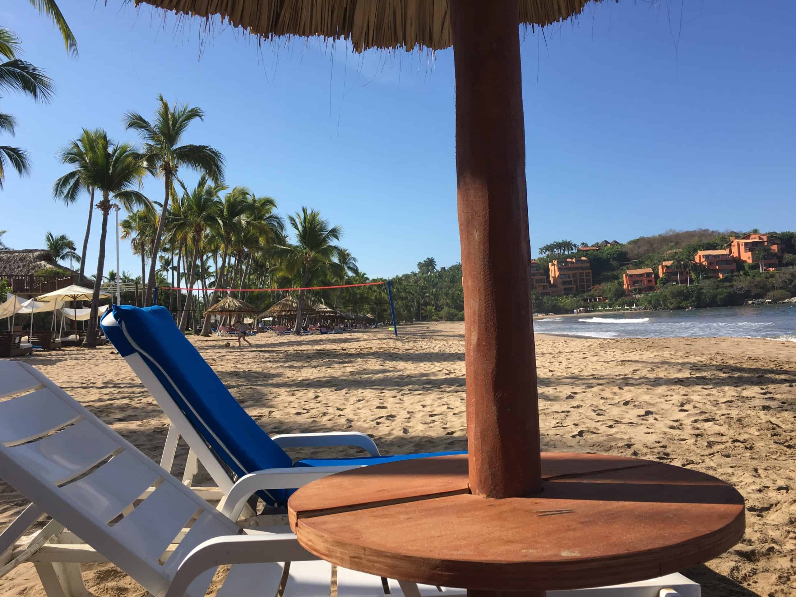 Chair and palapa on beach with hotels in background