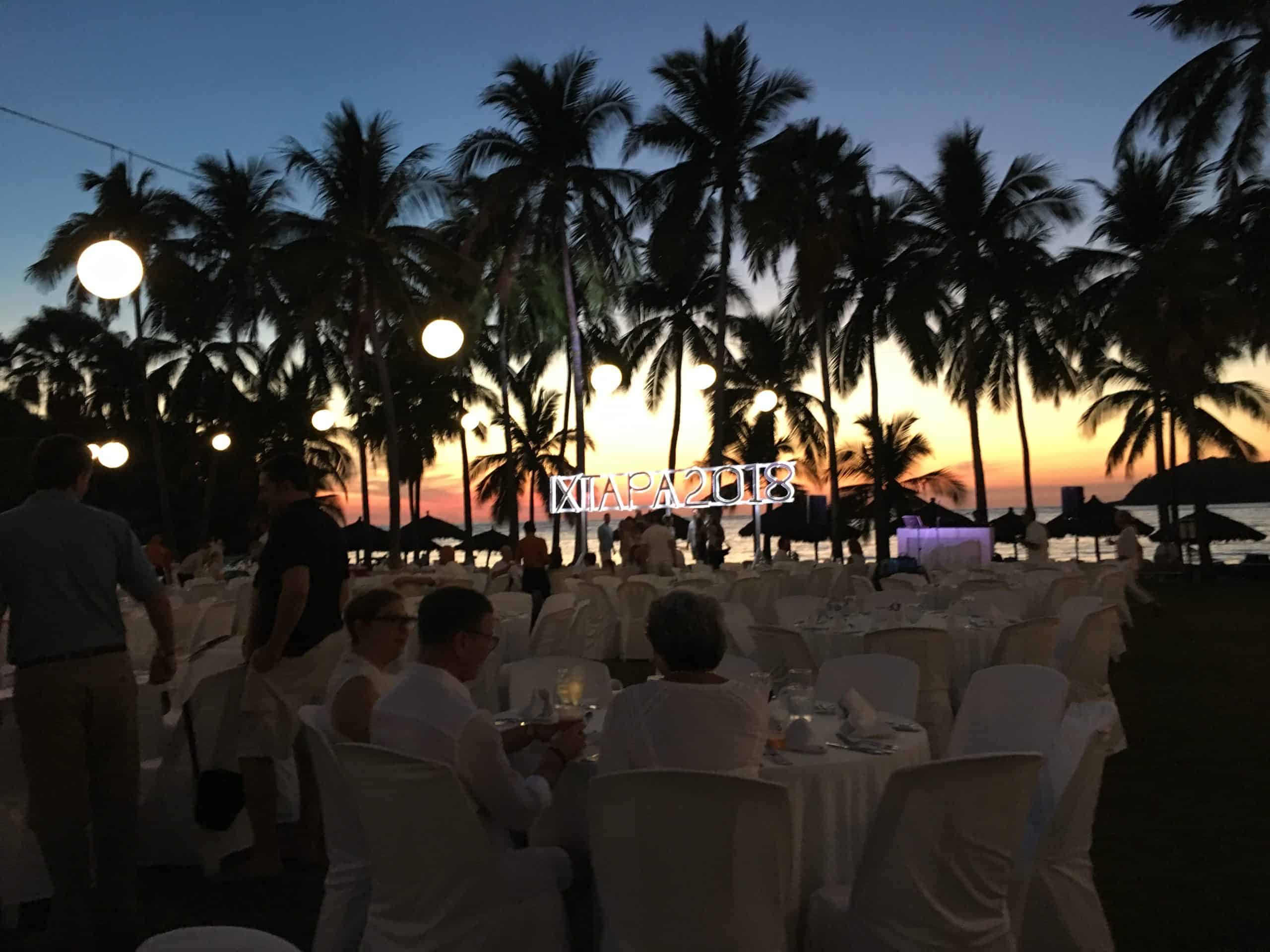 Sunset with palm trees and round tables with chairs covered in white linen