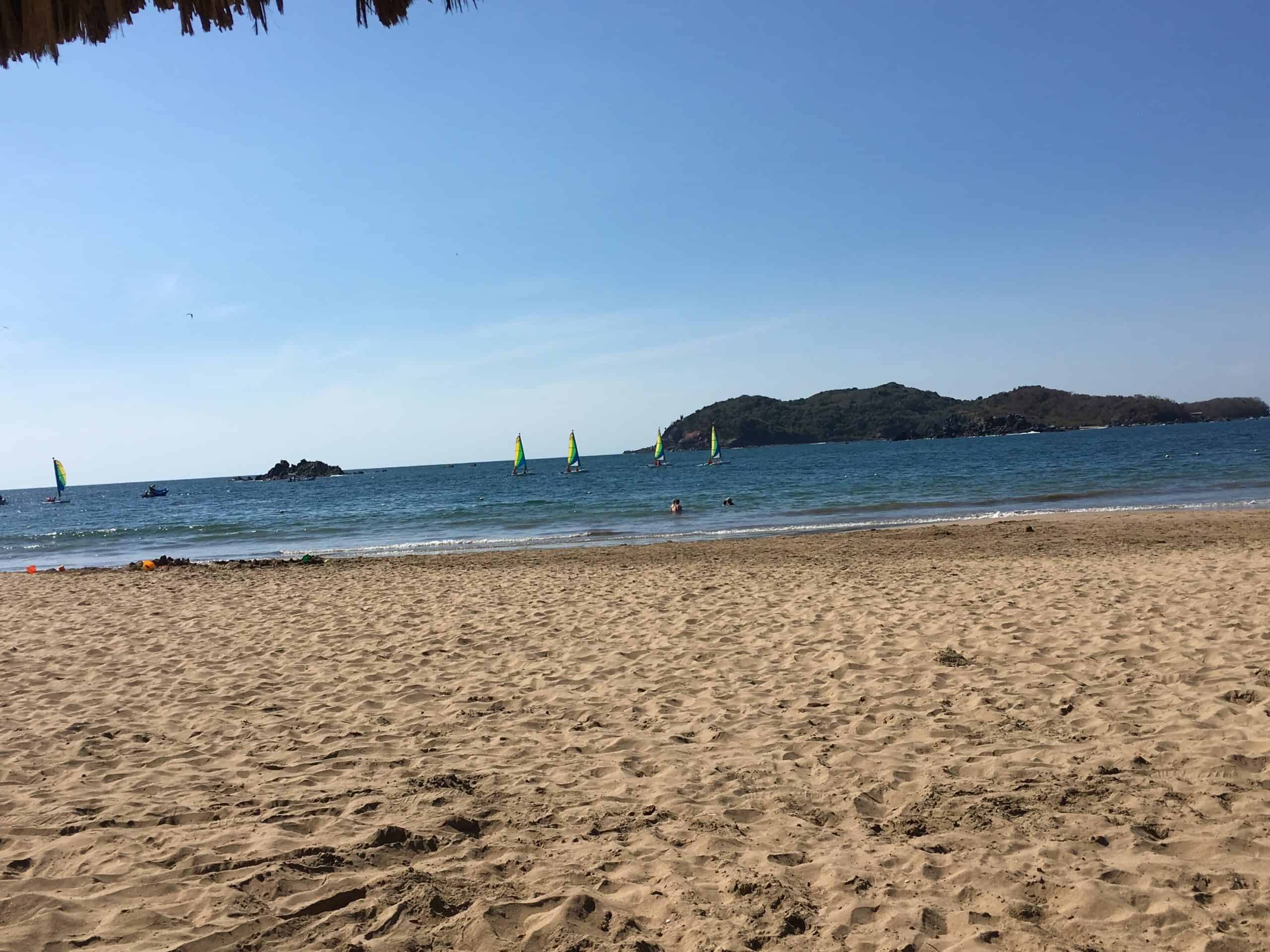 golden sand with sailboats in blue ocean water