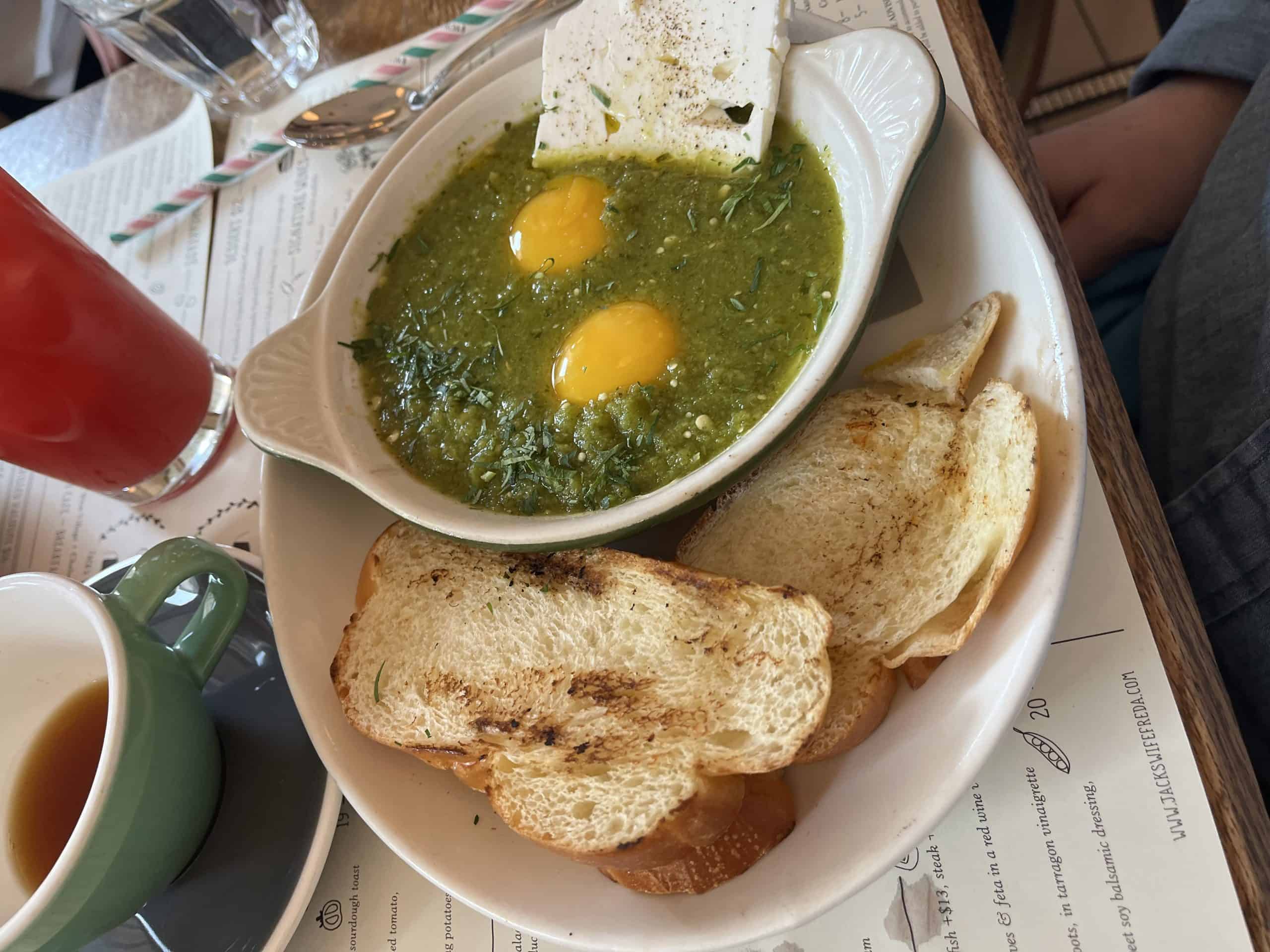 A bowl of green shakshuka with feta cheese on two pieces of bread on the side