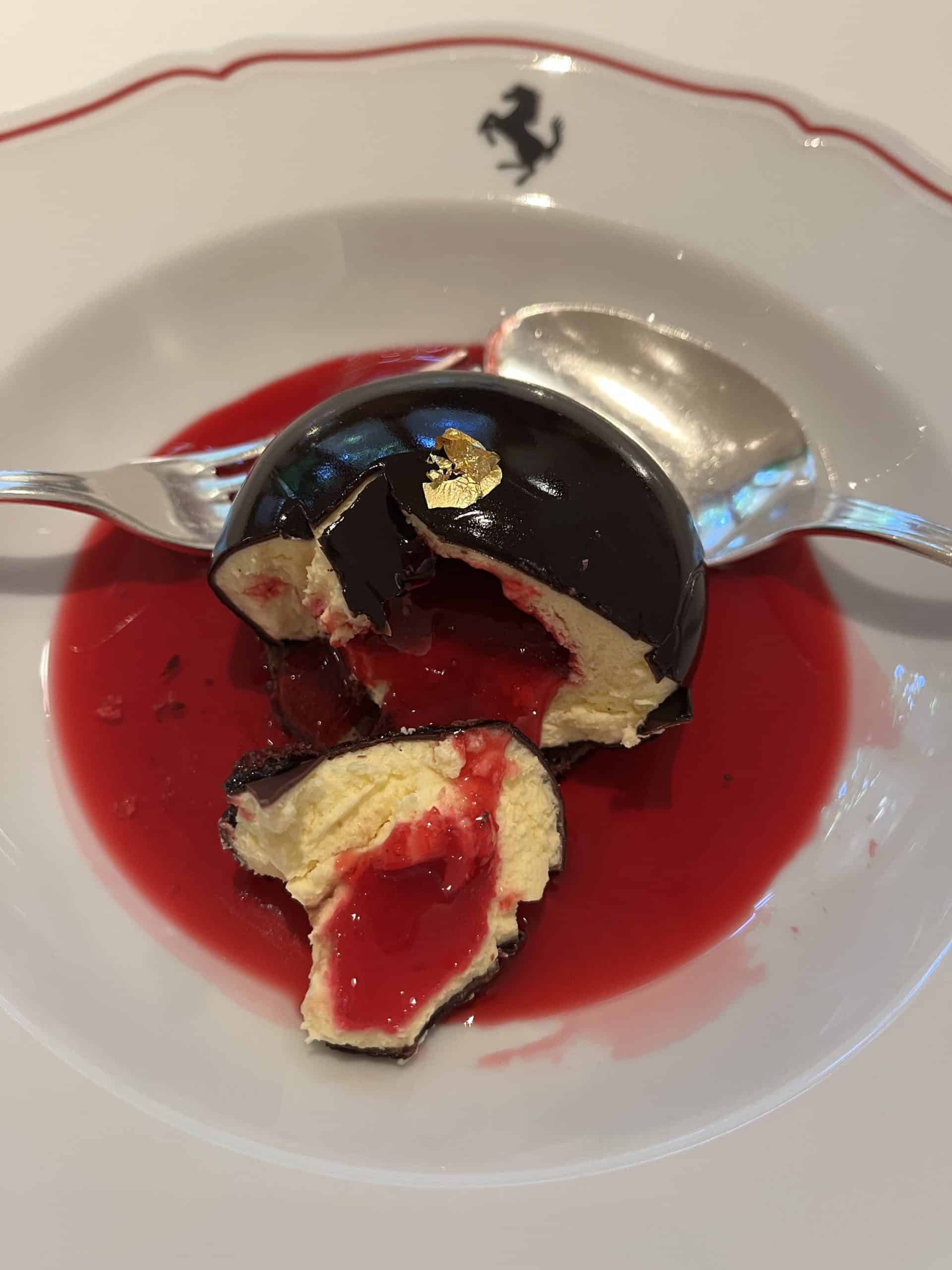 Decadent chocolate mousse dessert with berry sauce and gold leaf, served on a luxury Ferrari plate.