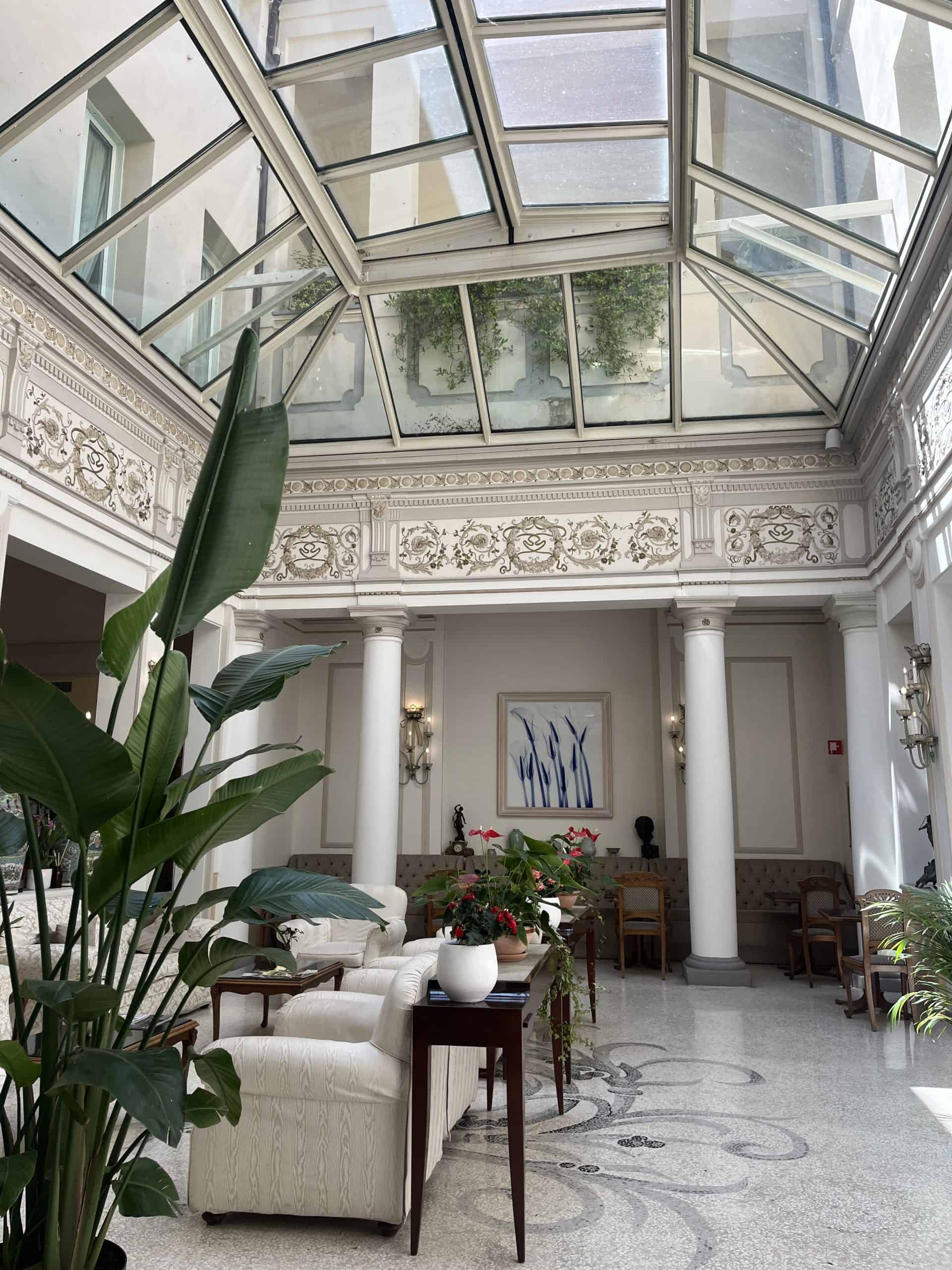 Bright hotel lounge featuring a glass ceiling and lush indoor plants.