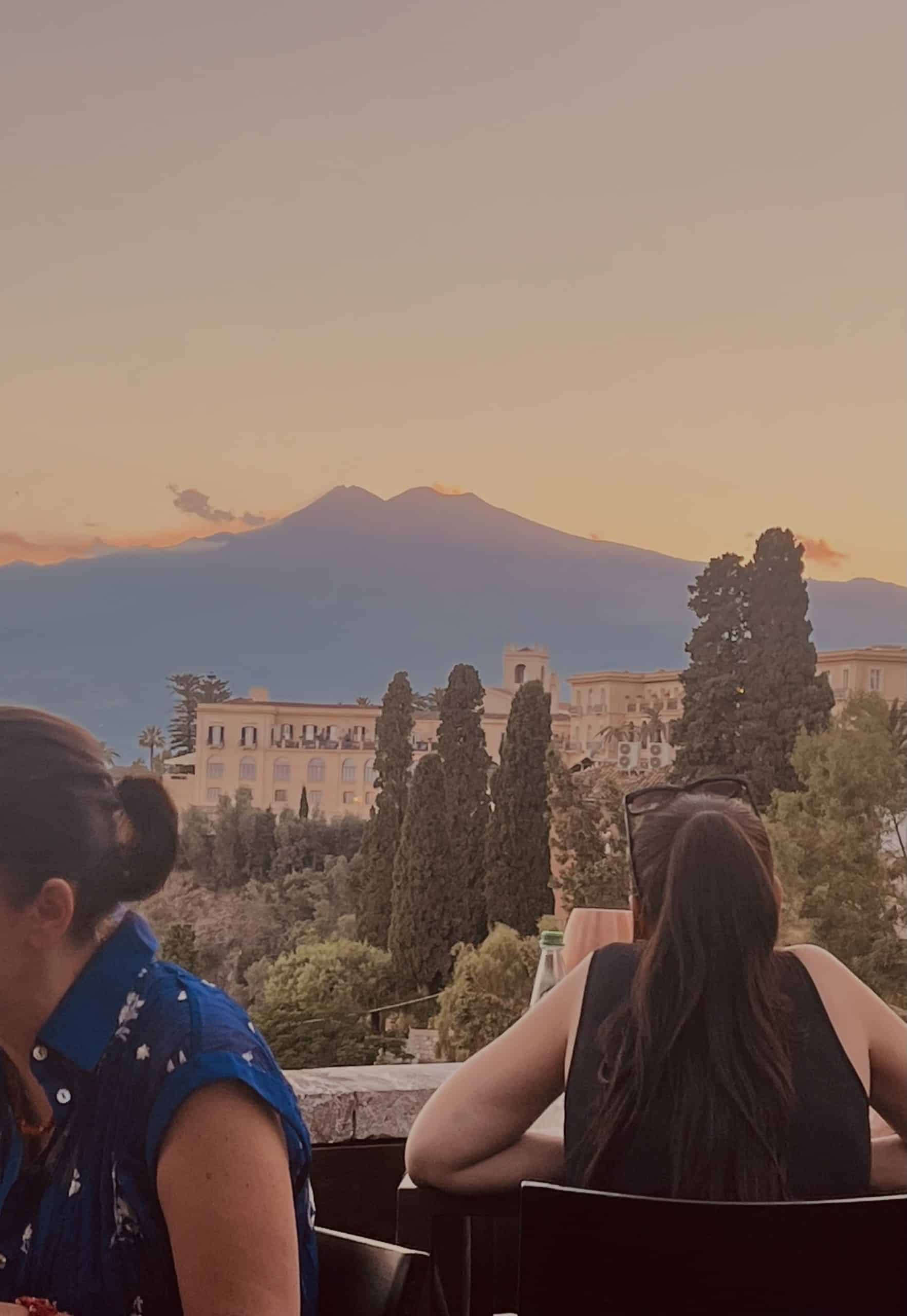 Mt. Etna in background as people sit outside in Taormina