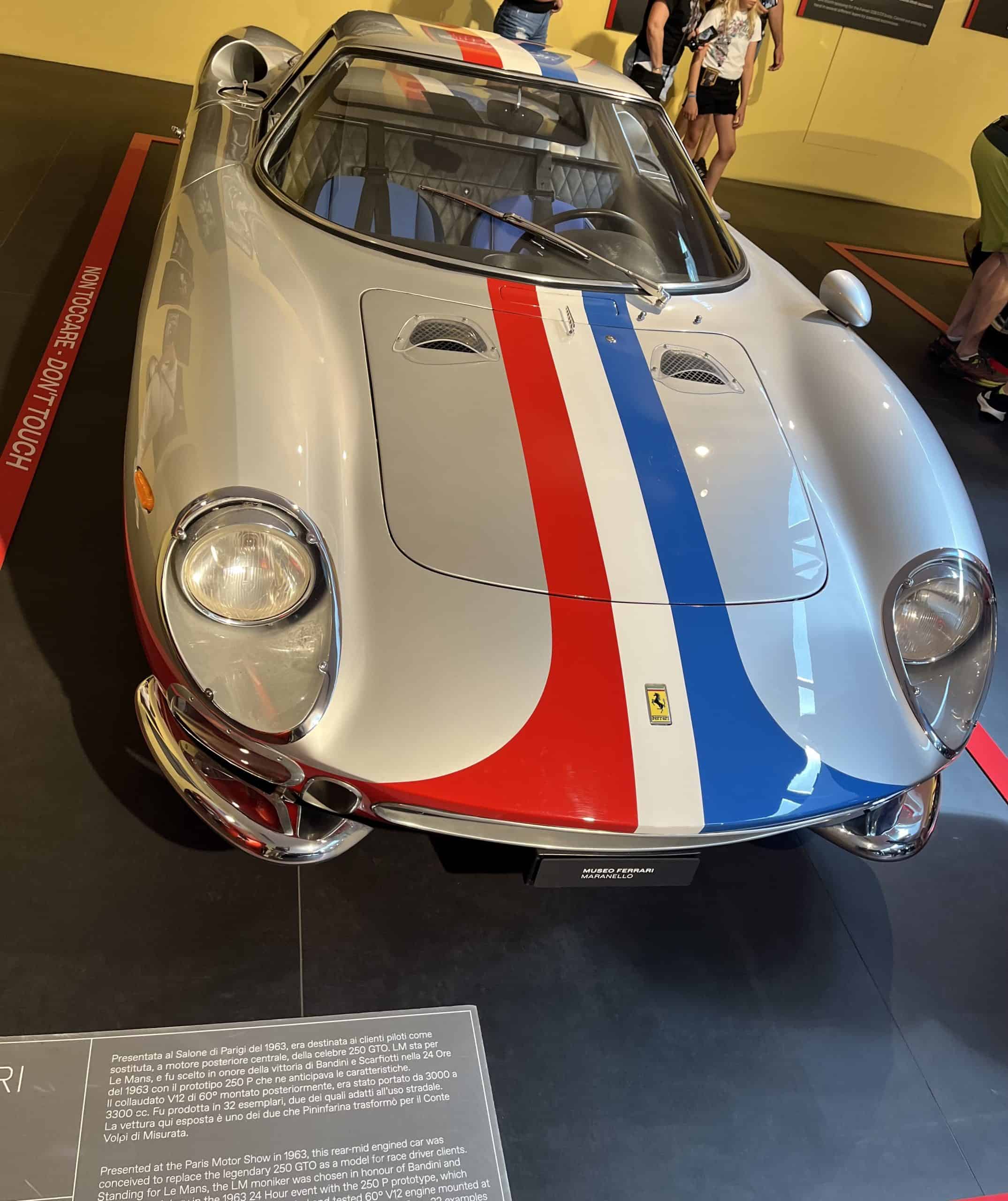 Ferrari 250 GTO race car with red, blue, and white stripes at a car museum.