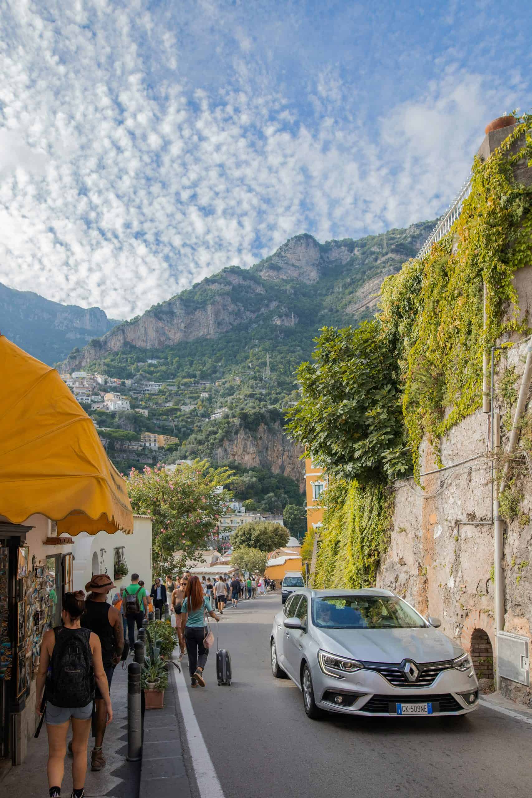 Tourists walking along Positano's street with mountains in background
