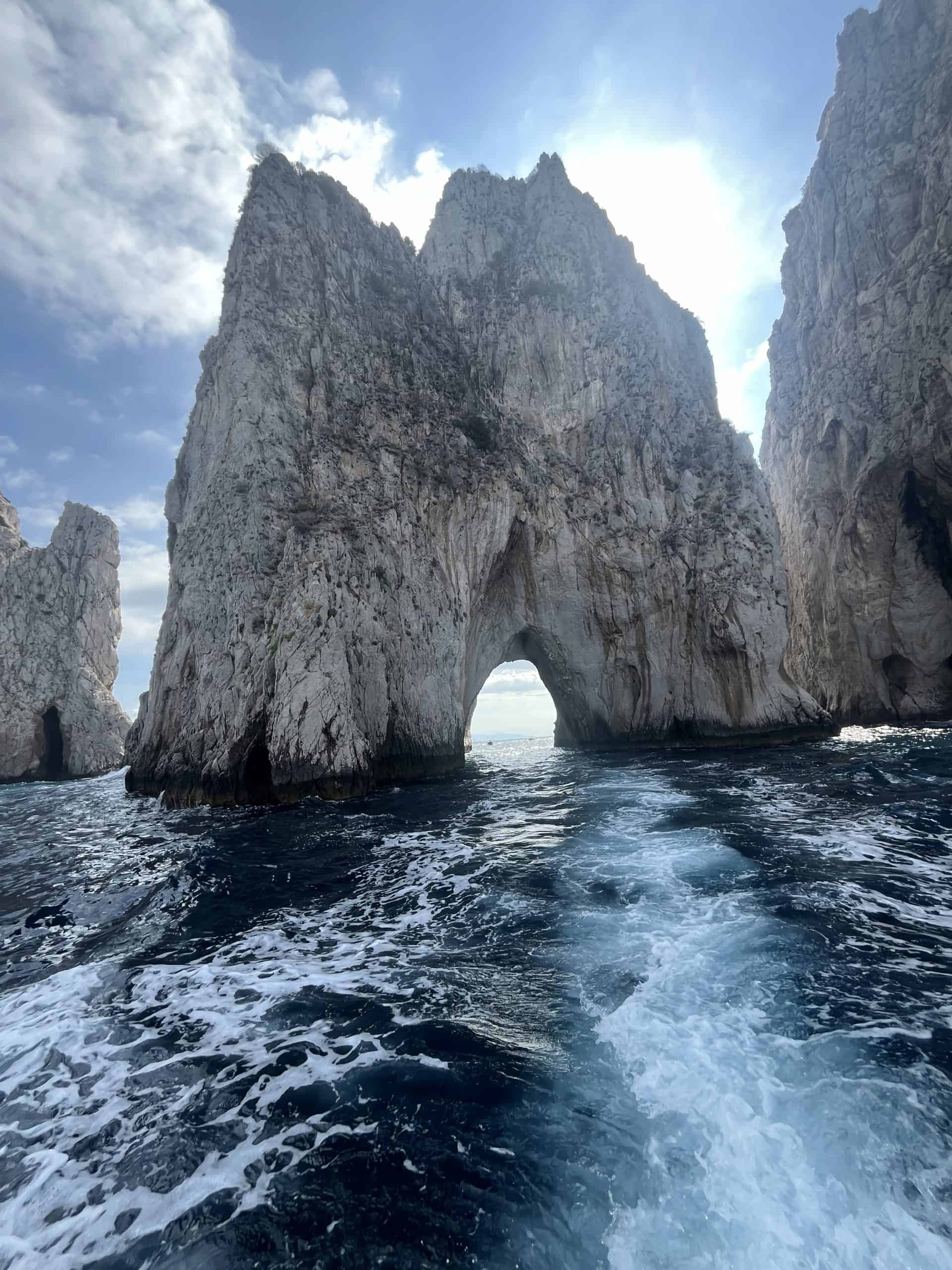 Up close view of the Faraglioni Rocks on water with sun shining in the background