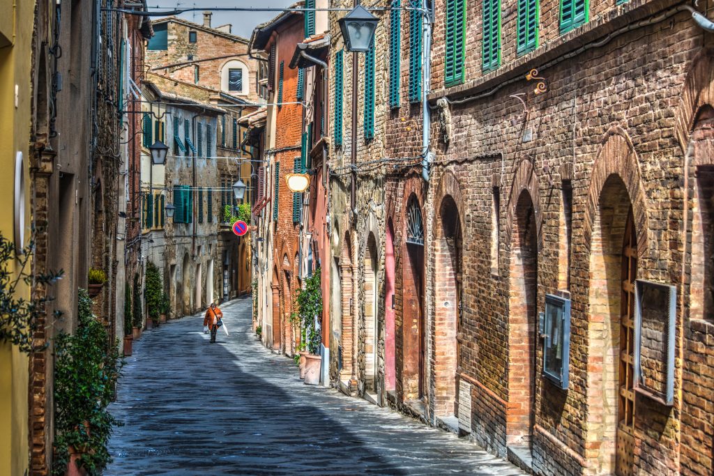 Woman walking down cobblestone narrow street and buildings in Montalcino