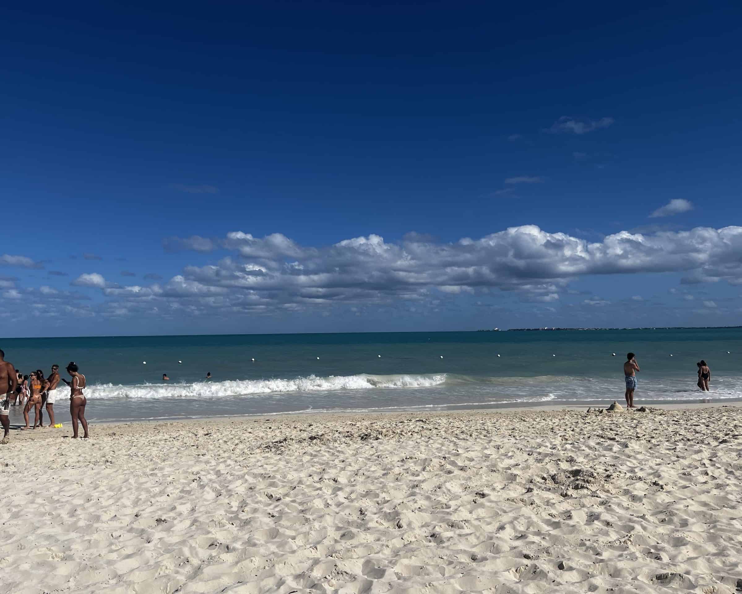 People walking on white sandy beach with blue ocean water in the background