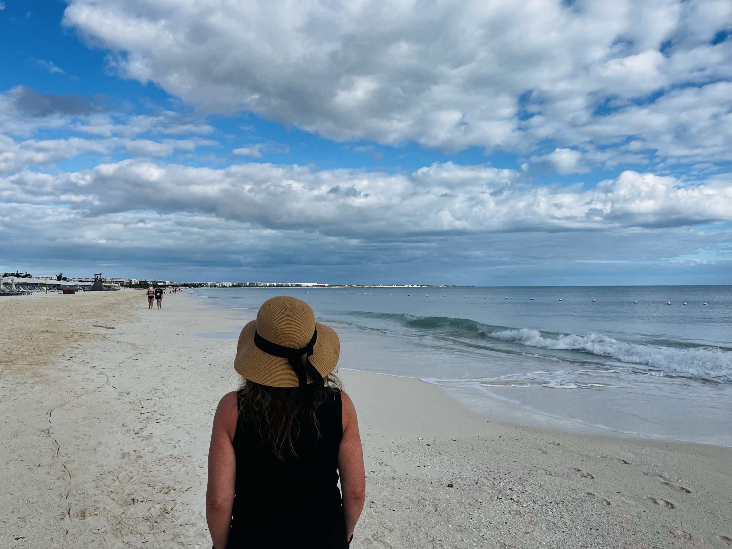 Person with a hat walking on the beach with blue sky and white clouds above