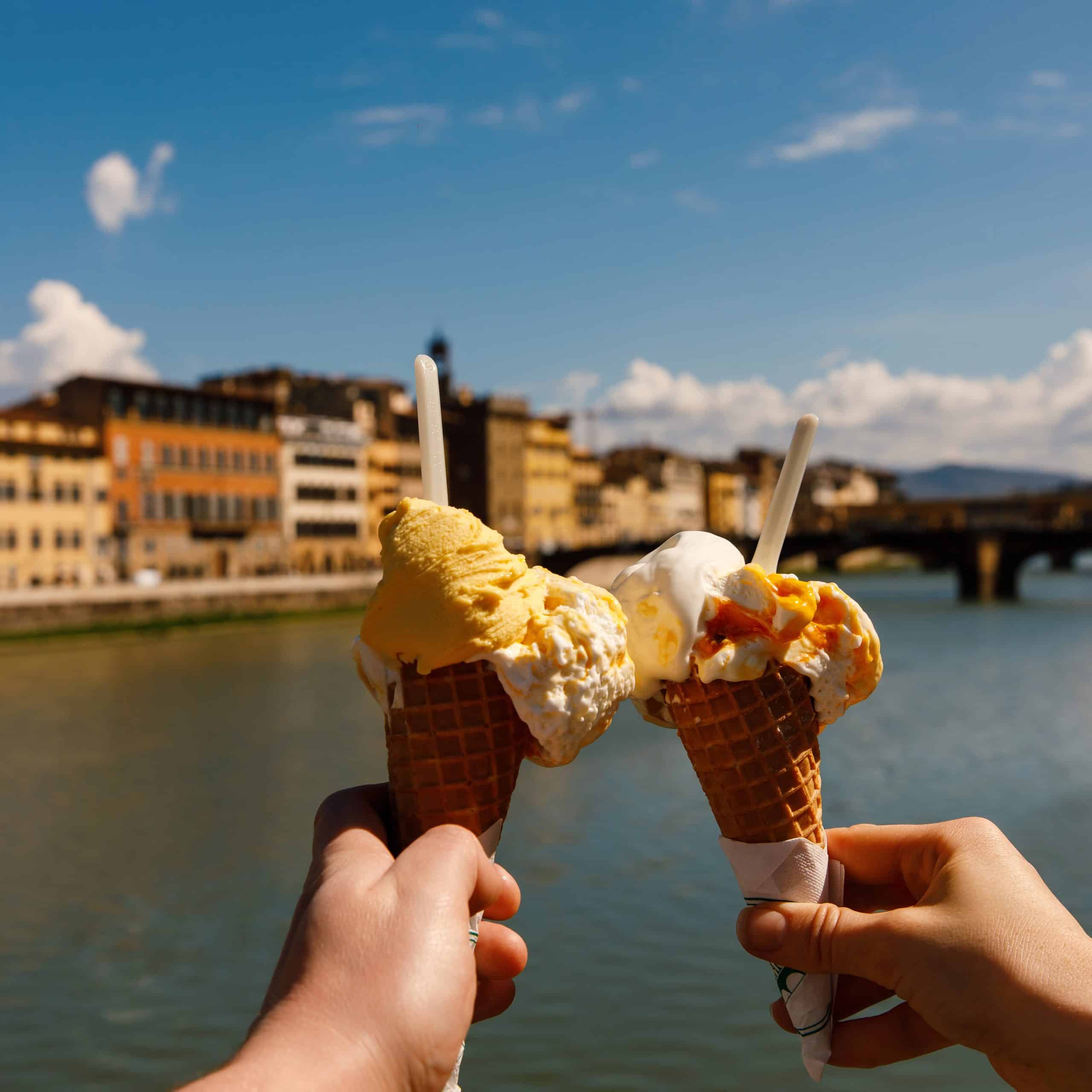 Two cones with gelato held with Arno River in background