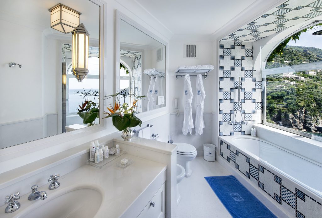 White and blue tile hotel bathroom with large tub and window overlooking cliff