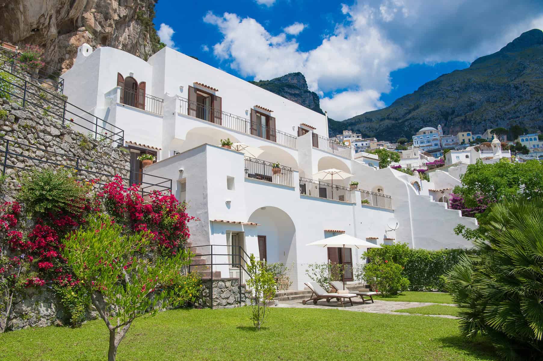 Seaside villa with white architecture, lush garden, and mountain backdrop
