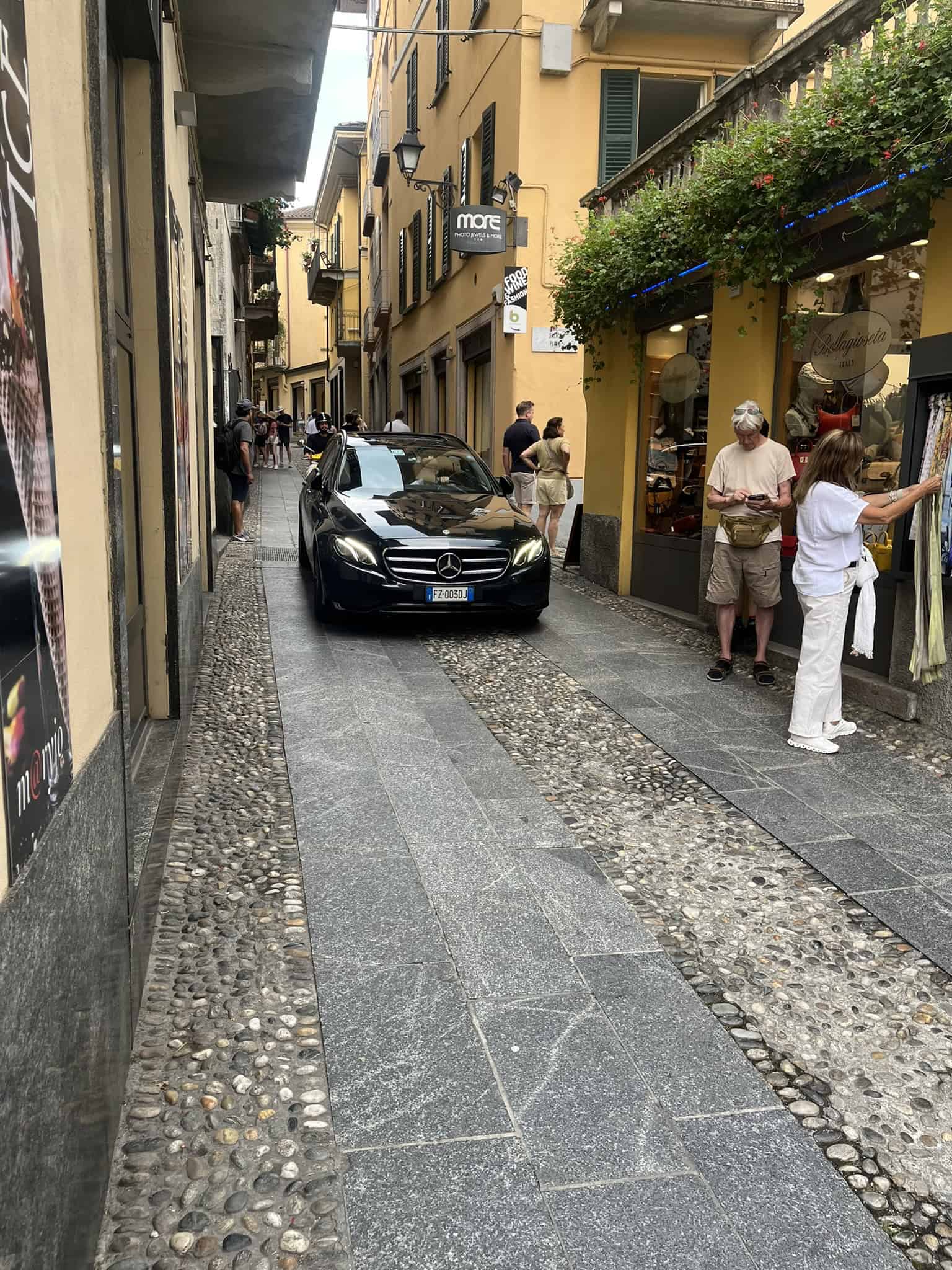 A car driving down a narrow road with stores and people on either side
