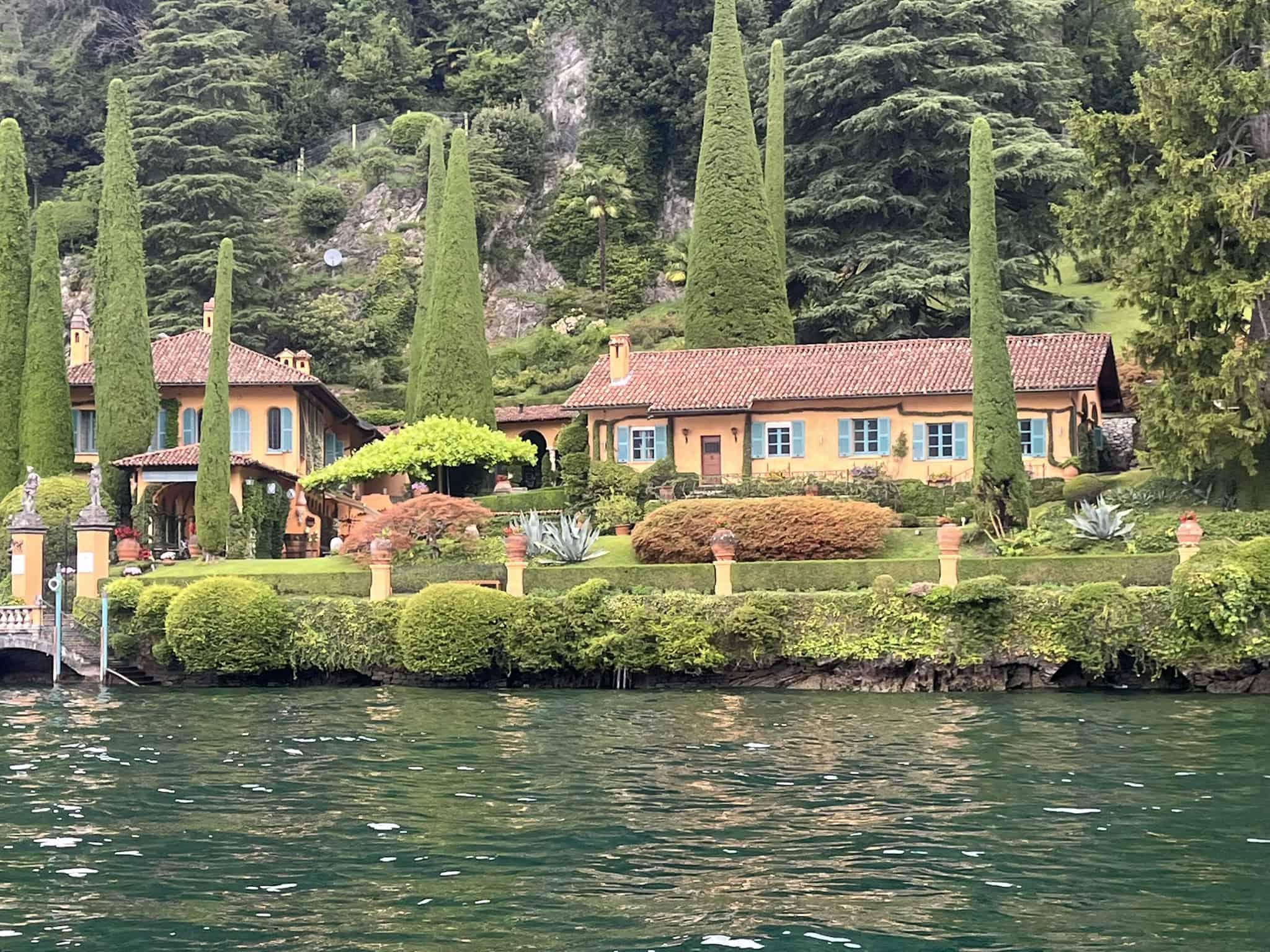 orange villa with red roof surrounded by cedar trees in a garden on the lake